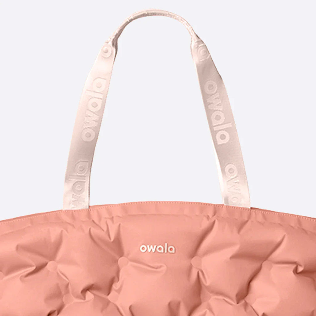Close-up of the Owala Cloud tote in Rosewood, coral pink puffer-quilted body with blush owala-tape handles featuring repeating Owala logo and Owala logo on the body